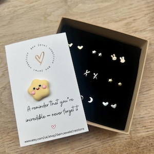 Caja de regalo con mensaje personalizado con 9 pares de pequeños aretes de plata o oro. Incluye un mensaje sentimental de su elección y un abrazo de bolsillo