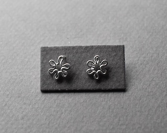 May include: A pair of silver stud earrings with a delicate, starburst design. The earrings are displayed on a black background.