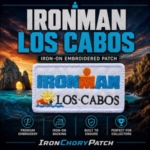 May include: A rectangular embroidered iron-on patch featuring the blue and orange Ironman logo with the text LOS CABOS in black. Below the logo is a yellow sun, a small orange rock formation, a cactus, and a blue wave on a white background.