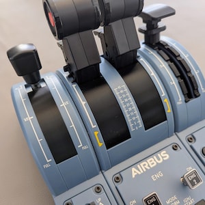May include: Close-up of a blue and black aircraft engine control panel with a lever, dials, and switches. The panel is labeled "AIRBUS" and has the text "ENG" and "MODE" printed on it.