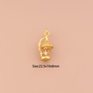 May include: A gold-colored pendant in the shape of a miniature lamp. The lamp features a detailed lampshade, a star-shaped base, and a clear gemstone. The size is 22.5x10x8mm.
