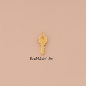 May include: A small, gold-colored key pendant with a loop at the top. The key measures 0.65 x 0.24 x 0.06 inches. The pendant is set against a soft, peach-colored background. The text "Size: 16.5x6x1.5mm" is visible.