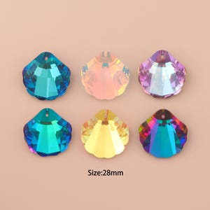Op de afbeelding: Zes iriserende, gefacetteerde kristallen schelpenhangers in tinten blauw, roze, paars en geel. Elke hanger heeft een gat aan de bovenkant om te rijgen. Afmeting: 28 mm.