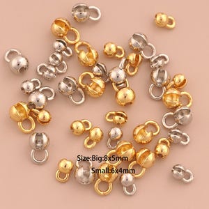 May include: A collection of gold and silver-colored jewelry findings, including ball-shaped clasps with attached loops. The image also includes text indicating the sizes: Big: 8x5mm and Small: 6x4mm. These findings are suitable for jewelry making.