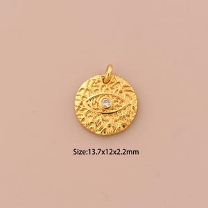 Puede incluir: Pendiente de encanto dorado con un diseño de ojo y un strass transparente en el centro. El pendiente mide 13,7 mm de ancho, 12 mm de alto y 2,2 mm de grosor.