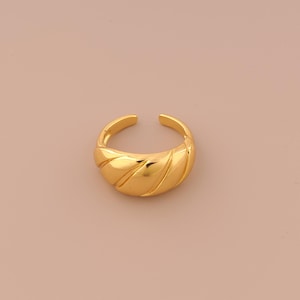 Puede incluir: Un anillo de color dorado con un diseño texturizado y curvo. El anillo está hecho de metal y tiene un acabado liso y pulido.