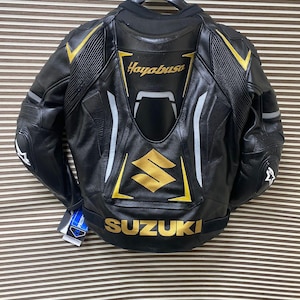 May include: Black leather motorcycle jacket with gold and white accents. The jacket features the words "Hayabusa" and "SUZUKI" on the back.