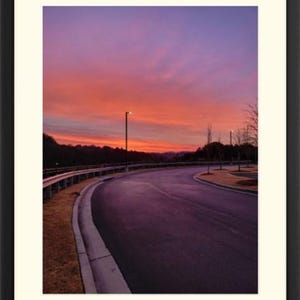 May include: A winding road curves through a suburban neighborhood at sunset. The sky is a vibrant mix of pink, purple, and orange, creating a beautiful and peaceful scene.