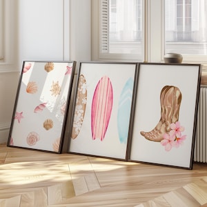 May include: Three framed prints with watercolor illustrations. The first print features seashells and starfish on a white background. The second print shows three surfboards in pink, blue, and white. The third print depicts a brown cowboy boot with pink flowers.