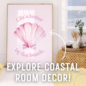 May include: A pink and white watercolor seashell with the text "Life's better by the beach." on a pink background. The image is framed and hanging on a wall.