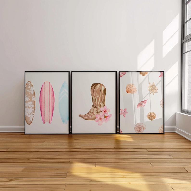 May include: Three framed watercolor prints. The first print features two surfboards with pink, blue, and white designs. The second print features a brown cowboy boot with pink flowers. The third print features a white background with a pattern of seashells and a starfish.