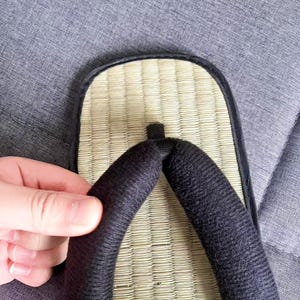 May include: Close-up of a traditional Japanese geta sandal. The sandal features a woven straw footbed, a black fabric thong, and a black border. The sandal is designed for outdoor wear and is a common part of Japanese attire.