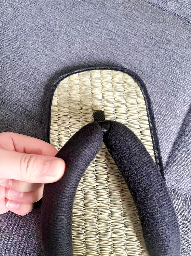 May include: Close-up of a traditional Japanese geta sandal. The sandal features a woven straw footbed, a black fabric thong, and a black border. The sandal is designed for outdoor wear and is a common part of Japanese attire.