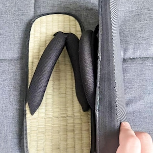 May include: A pair of traditional Japanese geta sandals. The sandals feature a natural woven straw footbed, black straps, and a black sole. The geta are designed with a raised platform for comfort and are suitable for casual wear.