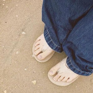 Może przedstawiać: Osoba w niebieskich dżinsach i beżowych sandałach z białymi paskami, odpoczywająca na piaszczystej plaży. Zdjęcie zrobione z g&oacute;ry, pokazujące stopy i dolne nogi.