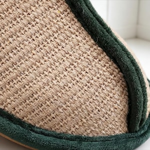 Pu&ograve; includere: Primo piano di una pantofola beige intrecciata con finiture verde scuro. La pantofola ha un aspetto strutturato in fibra naturale, che suggerisce comfort e abbigliamento casual. La finitura verde aggiunge un bordo a contrasto.