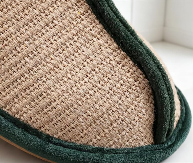 Pu&ograve; includere: Primo piano di una pantofola beige intrecciata con finiture verde scuro. La pantofola ha un aspetto strutturato in fibra naturale, che suggerisce comfort e abbigliamento casual. La finitura verde aggiunge un bordo a contrasto.