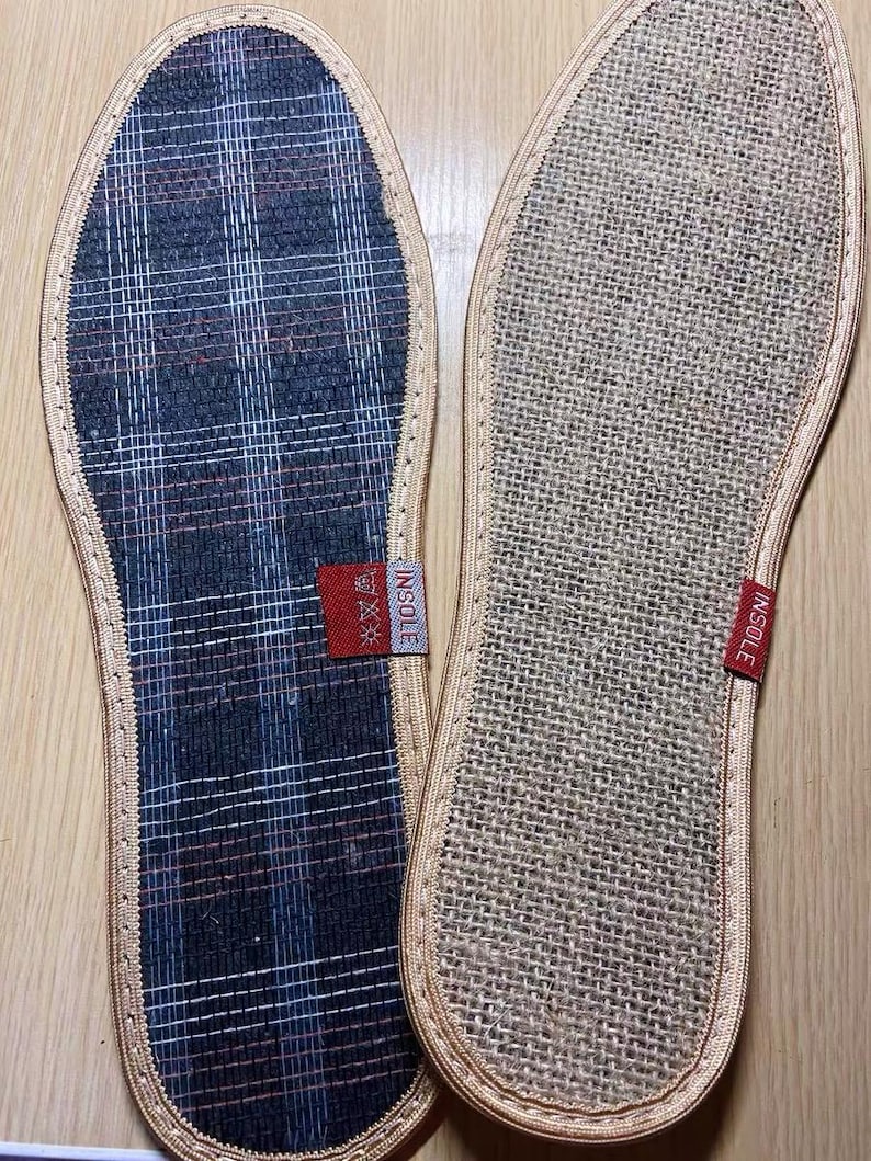May include: Two shoe insoles. One insole has a navy blue, red, and white plaid pattern. The other insole is a beige woven material. Both insoles have a beige border and a red tag that says "INSOLE".