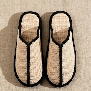Pu&ograve; includere: Un paio di pantofole beige intrecciate con finiture nere. Le pantofole hanno un design semplice a punta aperta e sono realizzate in un materiale strutturato. Le finiture nere delineano i bordi e l'apertura delle pantofole.