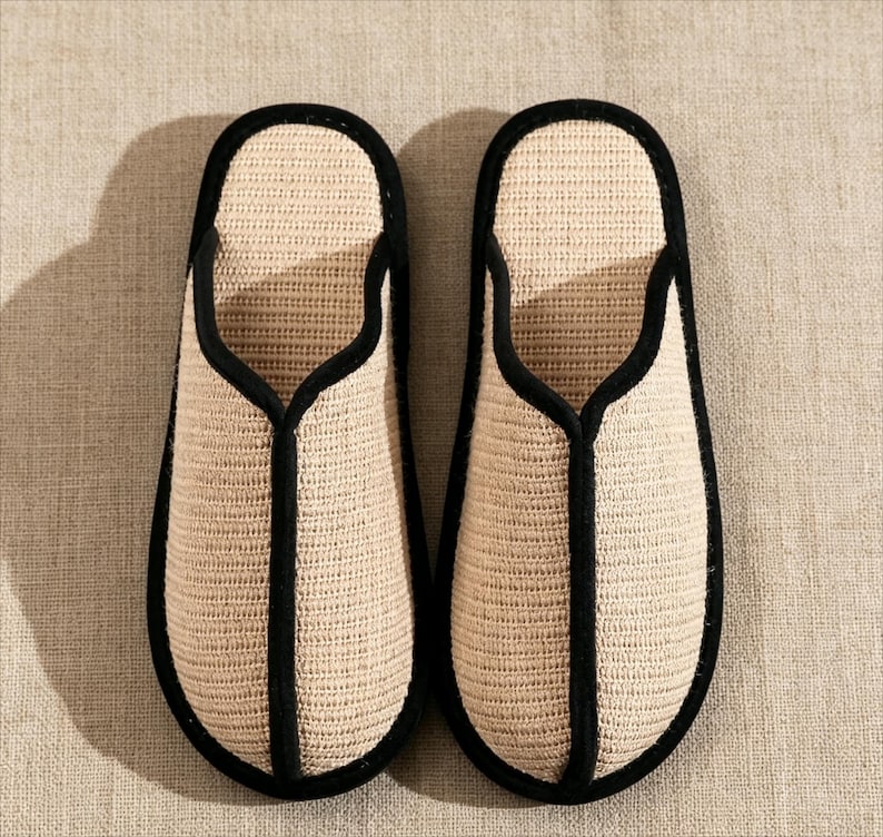 Pu&ograve; includere: Un paio di pantofole beige intrecciate con finiture nere. Le pantofole hanno un design semplice a punta aperta e sono realizzate in un materiale strutturato. Le finiture nere delineano i bordi e l'apertura delle pantofole.