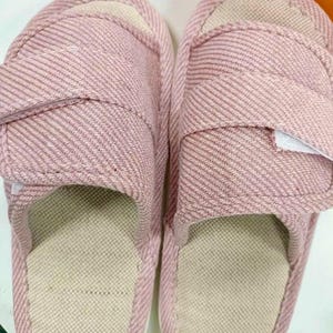May include: A pair of pink fabric slippers with a striped pattern. The slippers have a beige insole and an adjustable strap. The design is simple and comfortable, suitable for indoor wear.