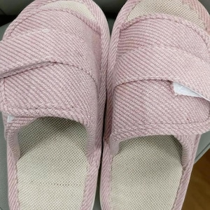 May include: A pair of pink adjustable slippers with a textured fabric. The slippers have a light beige interior and a hook-and-loop closure for a secure fit. The sole is a light beige color.