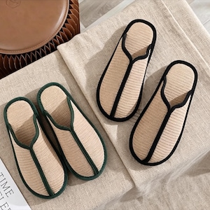 Pu&ograve; includere: Due paia di pantofole beige e nere con una trama intrecciata. Un paio ha un bordo verde scuro. Le pantofole sono disposte su un tessuto di colore neutro, suggerendo un focus sul comfort e l'uso domestico.