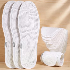 May include: White shoe insoles with a perforated design are displayed. Three insoles are laid out, with a stack of additional insoles and a rolled-up insole also visible. The insoles are made of a soft, breathable material.
