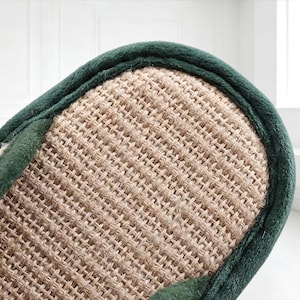 Pu&ograve; includere: Primo piano di una pantofola beige intrecciata con un bordo verde scuro. La superficie della pantofola presenta un motivo strutturato a tratteggio incrociato. Il bordo verde scuro borda il bordo della pantofola, fornendo un accento di contrasto.