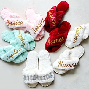 Puede incluir: Una colección de pantuflas afelpadas y personalizadas en varios colores. Se muestran pantuflas rosas, verde menta, rojas y blancas, cada una bordada con nombres o la palabra "Ride" en hilo dorado o plateado. Las pantuflas tienen un diseño de correa cruzada.