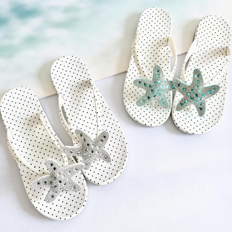 May include: White flip-flops with black polka dots, adorned with a starfish design. The starfish are embellished with silver and turquoise-colored rhinestones. The flip-flops are a summer accessory.