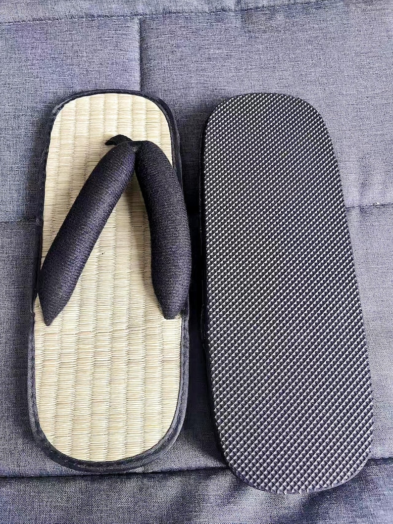 May include: A pair of traditional Japanese geta sandals. One sandal features a woven straw footbed with black straps, while the other displays a black rubber sole with a textured pattern. The sandals are designed for outdoor wear.