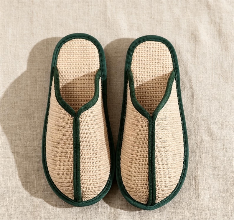 Pu&ograve; includere: Un paio di pantofole beige intrecciate con finiture verde scuro. Le pantofole hanno un design semplice a punta aperta e sono realizzate in un materiale di fibra naturale. La finitura verde delinea i bordi e l'apertura della pantofola.