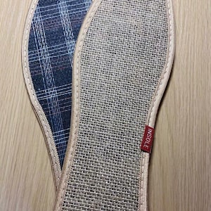 May include: Two shoe insoles. One is a woven beige material with a red tag that says "INSOLE". The other insole has a blue and white plaid pattern. Both insoles have a beige border.