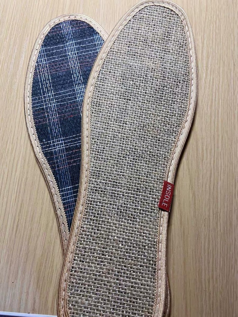 May include: Two shoe insoles. One is a woven beige material with a red tag that says "INSOLE". The other insole has a blue and white plaid pattern. Both insoles have a beige border.