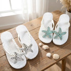 May include: White polka dot flip-flops with a starfish embellishment. The starfish is decorated with silver and turquoise rhinestones. The flip-flops are displayed on a wooden surface with seashells.