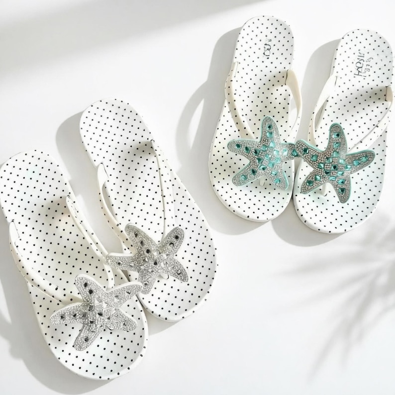 May include: White polka dot flip-flops with starfish embellishments. The flip-flops have a white thong strap and are decorated with a silver and turquoise starfish design. The flip-flops are a summer accessory.