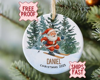 Peut inclure: Ornement de Noël rond avec le Père Noël skiant sur une pente enneigée, avec des sapins en arrière-plan. L'ornement porte le nom "Daniel" et l'année "2025". Il est suspendu par une ficelle.