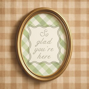 May include: Oval gold picture frame with a green and white checkered background. The frame contains the text "So glad you're here" in a cursive font.