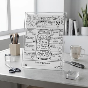 May include: A clear acrylic frame holding a white paper sheet titled All About My Dad Little Memories Edition. The sheet features a central jar illustration filled with hearts containing text, surrounded by eight numbered prompts for writing.