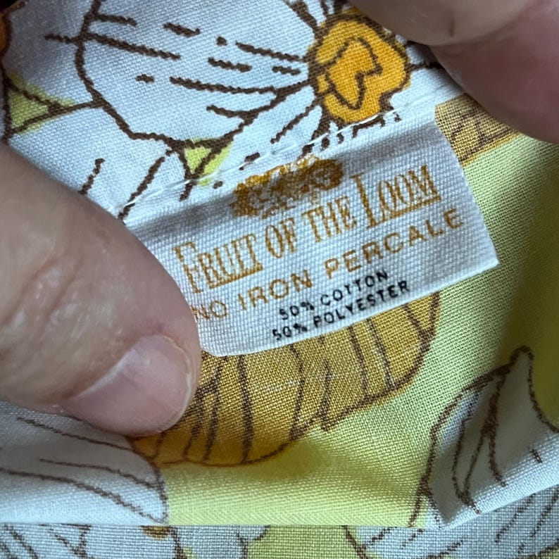 Pode incluir: Um tecido branco e amarelo com um padr&atilde;o floral marrom e amarelo. O tecido tem uma etiqueta que diz "Fruit of the Loom No Iron Percale 50% Algod&atilde;o 50% Poli&eacute;ster."