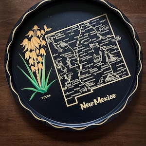 May include: A black round tray with a gold rim and a detailed map of New Mexico. The tray features illustrations of local flora and landmarks, with the word "Yucca" and "New Mexico" in gold lettering.
