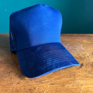 May include: A navy blue trucker hat with a mesh back. The hat has a curved brim and a solid front panel.