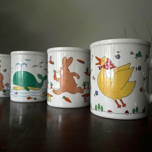 May include: A white ceramic mug with a black handle and the text "But First, Coffee" in a black, handwritten-style font. The mug is on a white surface.