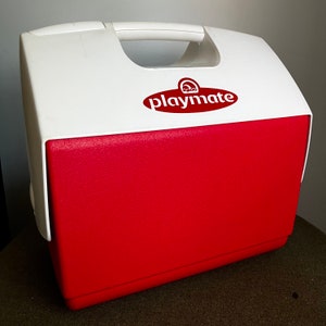 May include: A red and white Igloo Playmate cooler with a white lid and a red body. The cooler has a handle on the top and a logo that says "Igloo Playmate".