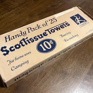 May include: A vintage box of Scottissue Towels, featuring the text "Handy Pack of 25." The box is beige with navy blue lettering and a circular emblem with the number "10¢." Additional text includes "For home uses," "Camping," "Touring," and "Pic-nicking."