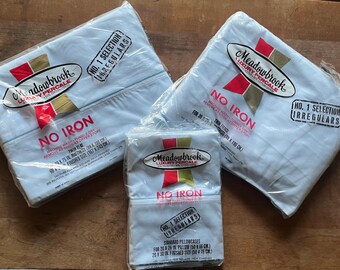 May include: Three packages of Meadowbrook Luxury Percale bed linens, including twin flat sheets and standard pillowcases. The packages are sealed in clear plastic and feature the text "No Iron" and "No. 1 Selection Irregulars".