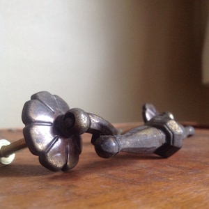 Puede incluir: Un tirador de cajón de latón vintage con un diseño floral y un tirador decorativo. El tirador está en un acabado desgastado y antiguo.