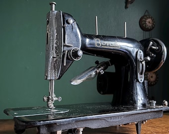 May include: A black vintage sewing machine with a metal foot pedal and a silver needle. The machine has a black metal arm with the word "Borne" written on it.