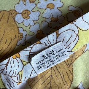 Pode incluir: Um tecido branco com fundo amarelo e um padr&atilde;o floral. O tecido tem uma etiqueta que diz "81 x 104 Size Before Hemming Machine Wash - Tumble Dry Remove at Once and Fold Made in U.S.A."
